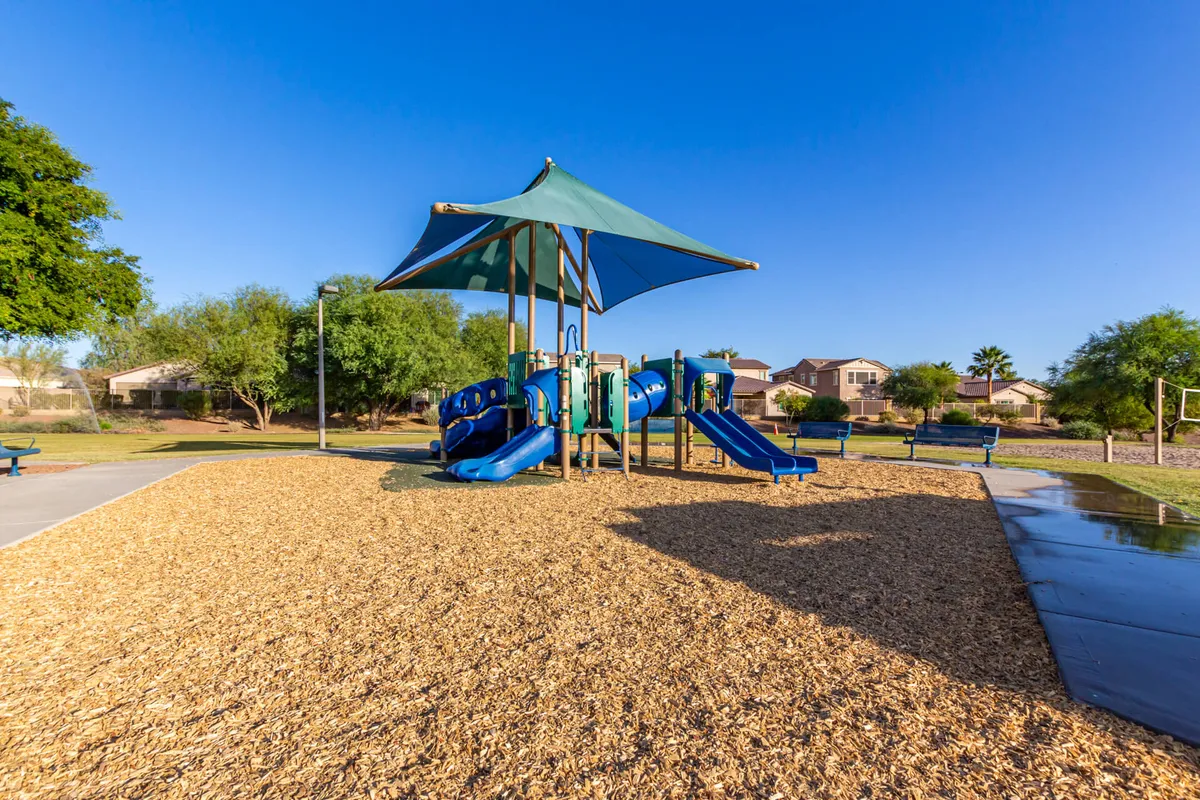 A cheerful playground scene featuring modern play structures, slides, and a shade canopy, with children playing and families gathering for picnics nearby. The area is vibrant and lively, embodying the spirit of family-friendly community amenities.