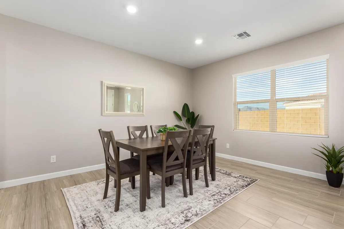 A cozy dining area featuring a large wooden table surrounded by chairs, a window providing natural light, a decorative mirror, and a touch of greenery with a potted plant. The scene feels warm and inviting, perfect for family meals and lively conversations.