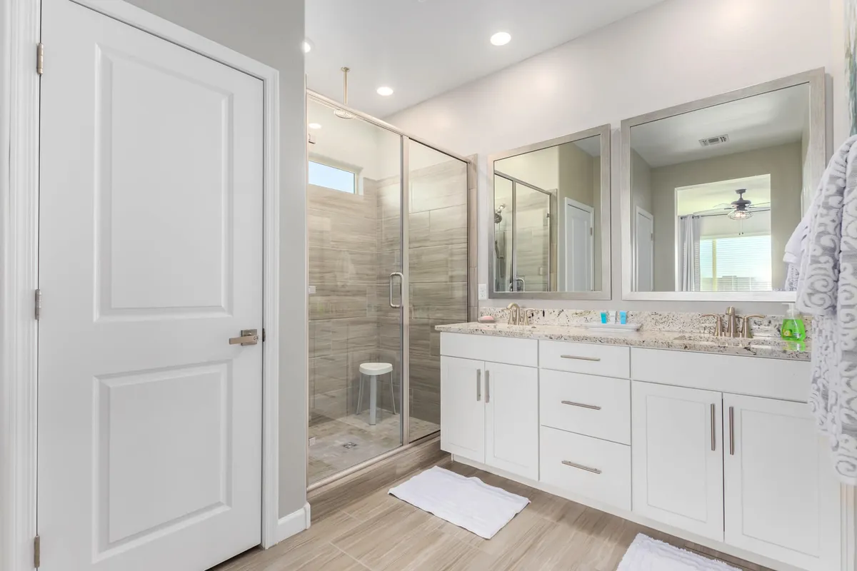 A modern, serene bathroom featuring large mirrors, a glass shower enclosure, and a double sink vanity. The space is bright, clean, and designed for both routine and relaxation.