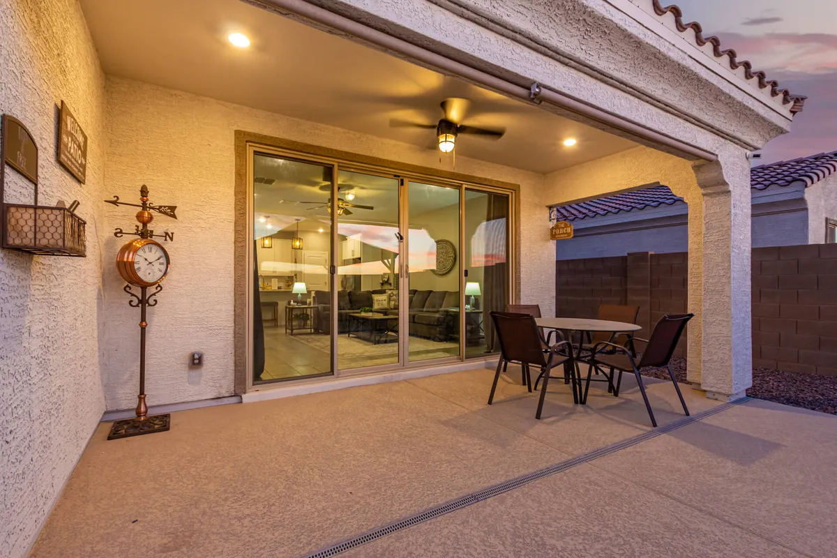 This image showcases a cozy outdoor seating area with a decorative clock and glass sliding doors, surrounded by lush greenery and patio furniture. The setting is ideal for relaxing, dining outside, or hosting a family barbecue in a private, sun-dappled oasis.