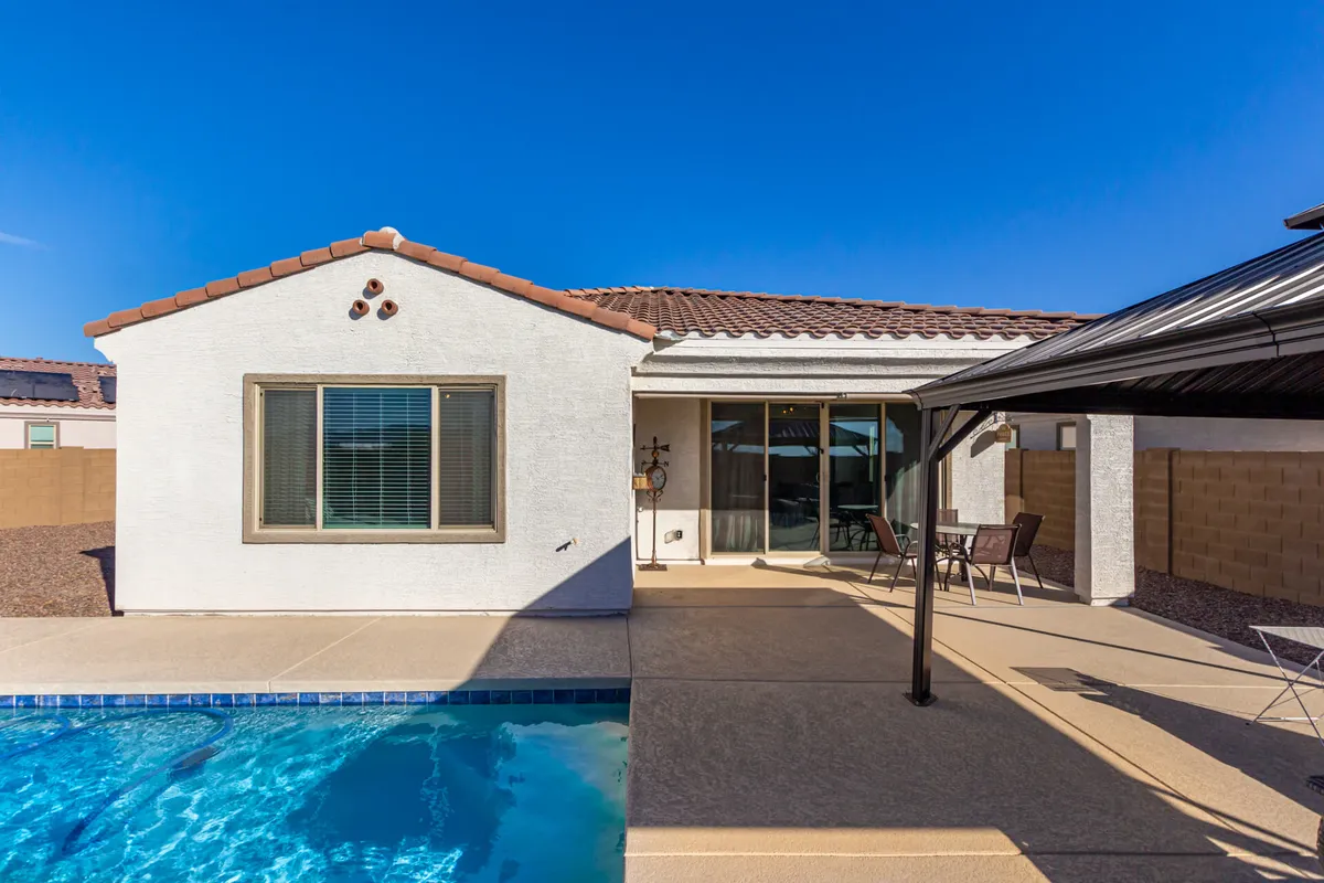 A sunny backyard featuring a refreshing pool, comfortable patio furniture, and seamless access to the home via sliding glass doors. The space is perfect for sunbathing, outdoor dining, and sharing memorable celebrations with friends and family.