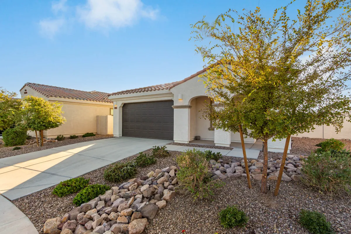 A welcoming front entrance with a landscaped garden, garage door, and inviting pathway. Seasonal flowers and greenery frame the entrance, suggesting a well-kept, vibrant home environment ideal for returning after a day out.