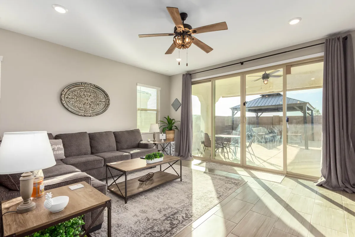 A comfortable living area with a plush sofa and coffee table set near large sliding glass doors, allowing abundant natural light to pour in. A ceiling fan and neutral color palette add to the sense of relaxation, making it an ideal spot for unwinding or socializing after a busy day.