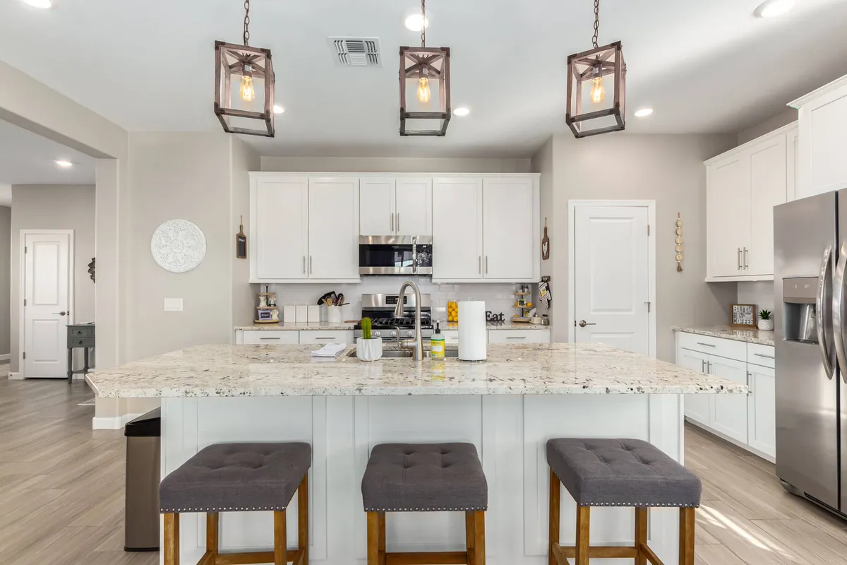A spacious kitchen with a prominent granite countertop, modern stools for casual seating, stylish lighting fixtures, and stainless steel appliances throughout. The layout encourages both food preparation and gathering, with a warm, welcoming ambiance ideal for entertaining.