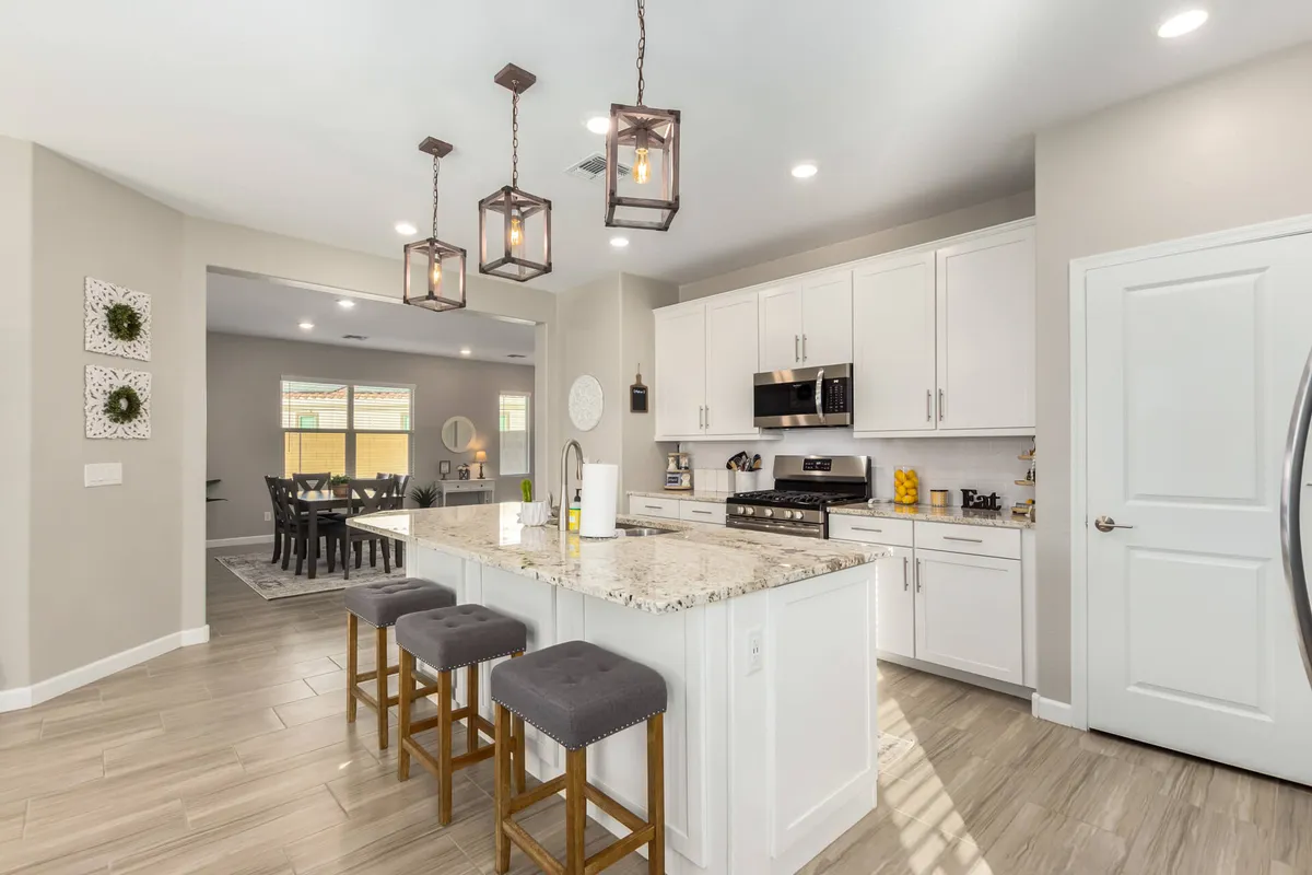 A bright kitchen scene showcasing a sleek granite countertop, pendant lights, and modern stainless steel appliances, with an adjacent dining area visible in the background. The setup is clearly tailored for both cooking and socializing, seamlessly connecting the kitchen and dining spaces.