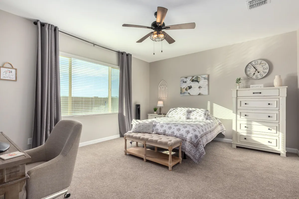 A calm and cozy bedroom with a soft bed, window flooding the space with natural light, a desk, dressing table, dresser, and decorative wall art. The room feels inviting, perfect for relaxing or getting a restful night’s sleep.