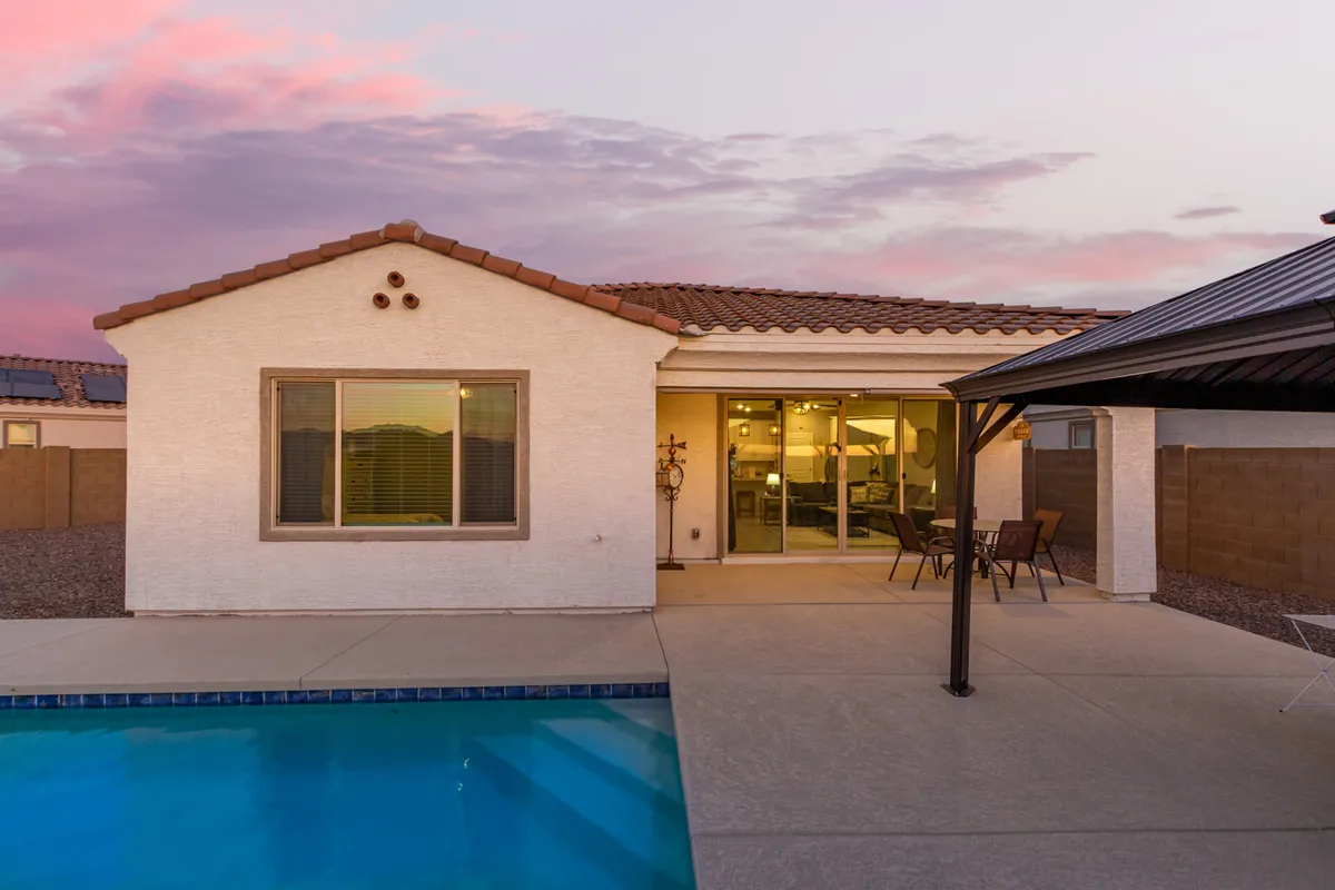 A tranquil pool and patio setting, with the house exterior in the background. The patio area features outdoor seating, inviting guests to relax, dine, or enjoy evening swims in a private and serene environment.