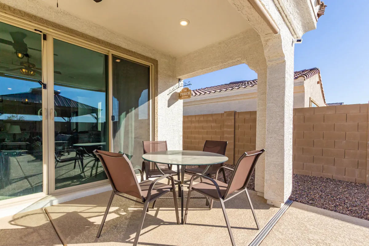 A cozy patio with a glass table, metal chairs, and decorative touches, including a 'porch' sign. The area is adjacent to sliding glass doors, providing a seamless connection between indoor comfort and outdoor enjoyment—perfect for morning coffee or al fresco dining.